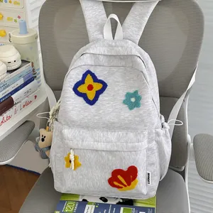 Close-up of grey school backpack with colorful flower embroidery and bear keychain