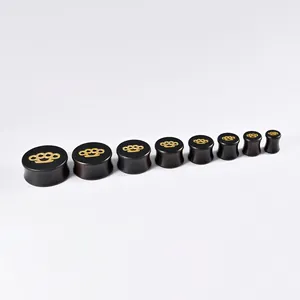 Close-up of black ebony wood ear gauges with decorative golden knuckle duster pattern inlay