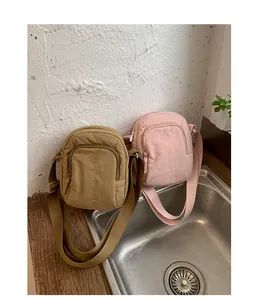 Zwei Mini-Umhängetaschen aus Nylon in Khaki und Rosa an einer strukturierten Wand.