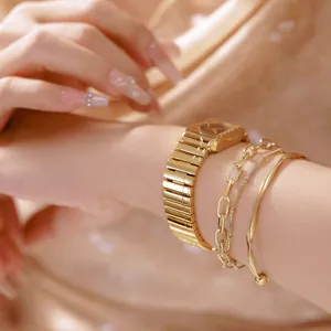 Elegante reloj vintage dorado con correa de piano y pulseras en la muñeca de una mujer.