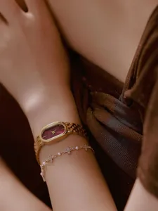 Detailansicht einer weinroten Vintage-Armbanduhr mit Goldband und Kleeblatt-Armband.