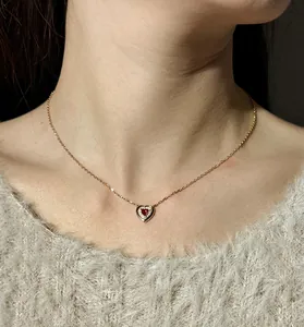 Close-up of an elegant rose gold heart pendant necklace with a red stone on a model
