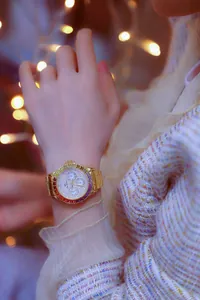 Close-up of a luxury gold women's watch with a rainbow crystal bezel on a wrist.