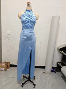Close-up of elegant light blue halter neck satin evening gown with ruched waist and high slit.