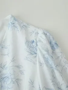 Dettaglio della stampa floreale blu e della manica a sbuffo su un abito bianco con scollo a V.