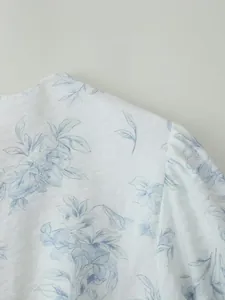 Dettaglio ravvicinato di eleganti motivi floreali blu su un abito estivo bianco con maniche a sbuffo