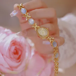 Detalle de reloj pulsera dorado Bee Sister con concha azul y accesorio de rosa rosada.