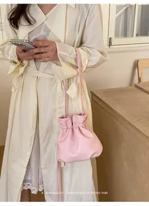 Detail shot of a minimalist pink drawstring crossbody bag styled with a cream coat