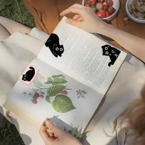 Detailed view of cute black cat magnetic bookmarks clipped to an illustrated book page.