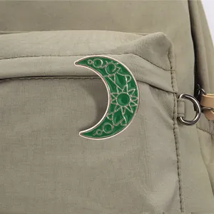 Detalle de un pin esmaltado de luna creciente verde en una mochila resistente verde oliva.