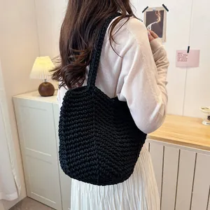 Back view of a black hand-woven crochet tote bag worn by a model in a cozy indoor setting