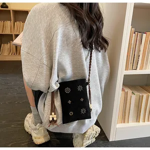 Close-up of a black velvet crossbody phone bag with beaded details and leather strap