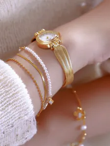 Primer plano de un elegante reloj dorado con correa de malla y pulseras de perlas