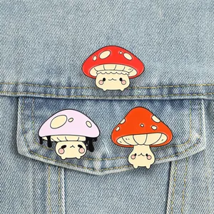 Detail showing three cute anthropomorphic mushroom enamel pins on a denim jacket pocket.