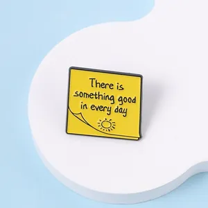 Detalle del pin de esmalte de nota adhesiva amarilla con frase inspiradora y un sol