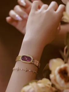 Nahaufnahme einer ovalen weinroten Vintage-Uhr und eines goldenen Armbands am Handgelenk