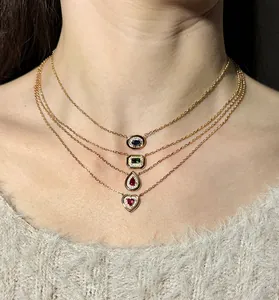 Close-up of four stacked gold-tone necklaces with heart and teardrop gemstone pendants.