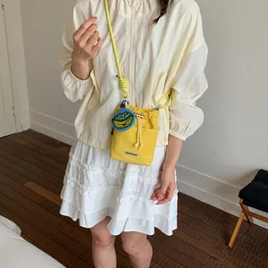 Yellow drawstring bucket bag with banana charm worn by a model in a casual setting