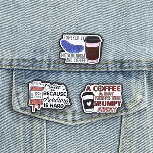 Detailed close-up of three funny coffee-themed enamel pins pinned to a light blue denim jacket