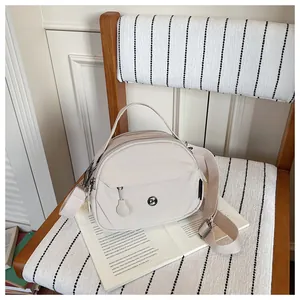 Vista detallada del elegante bolso bandolera de nailon beige en una silla con un libro