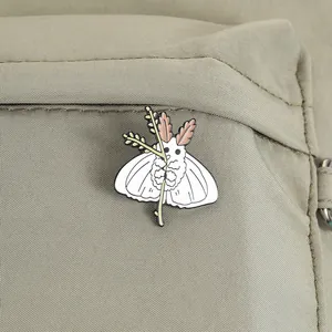Vue détaillée d'un pin's en émail de papillon de soie blanc sur un sac en toile vert.