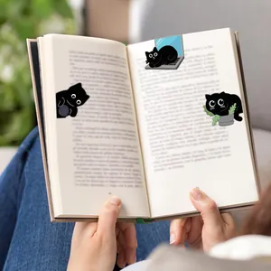 Three cute cartoon black cat magnetic bookmarks clipped on open book pages in detail