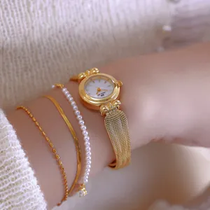 Primer plano de un elegante reloj vintage dorado para mujer con correa de espiga y pulseras