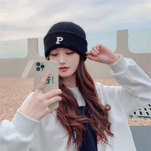 Fashionable black knitted beanie hat with white letter P embroidery worn by a model
