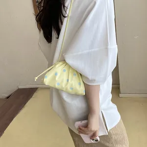 Detail view of a yellow gathered pouch bag with blue polka dots worn by a model