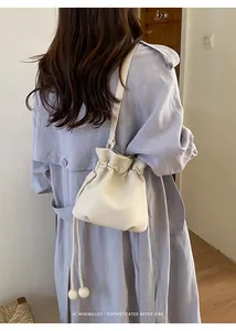 Beige leather drawstring bag with ball tassel detail shown on model in trench coat