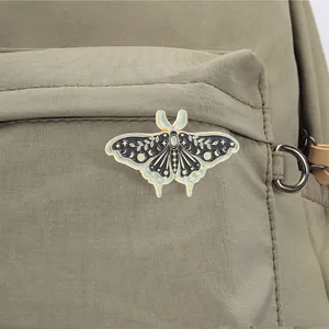 Detailed view of a vintage celestial moth enamel pin on a green canvas bag