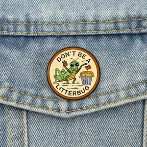 Gros plan sur un pin's en émail avec insecte sur denim, portant le slogan 'Don't Be A Litterbug'