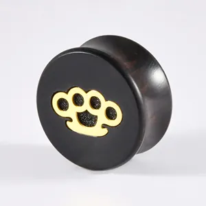 Macro view of black ebony wood ear plug featuring a detailed gold knuckle duster inlay