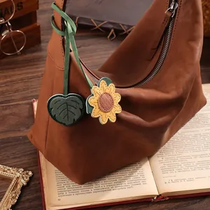 Vintage handcrafted leather sunflower and leaf bag charm hanging on a classic book