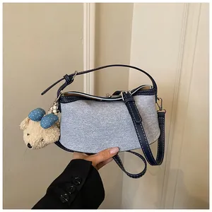 Detail view of light blue denim bucket bag with navy leather trim and bear charm