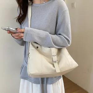 Detail view of minimalist cream faux leather hobo shoulder bag with buckle strap worn by model