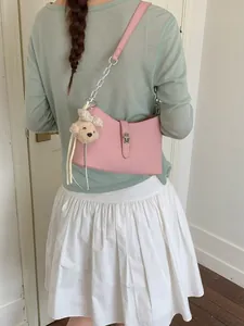 Fashionable pink leather underarm bag for women worn by a model with a cute bear charm