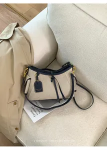 Bolso de hombro en lona beige y cuero azul marino sobre un elegante sofá blanco