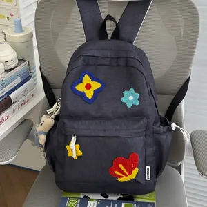 Close-up of a cute navy blue school backpack featuring colorful floral embroidery on a grey chair