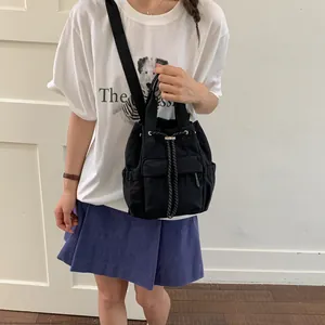 Primer plano de una mochila negra con cordón llevada por una modelo en un entorno casual