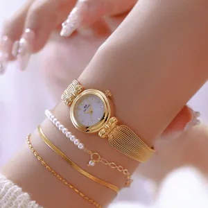 Primer plano de reloj vintage dorado con correa de malla espiga y pulseras de perlas.