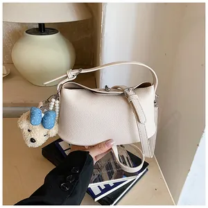 Elegant beige pebbled leather bucket bag with a cute teddy bear charm held by hand