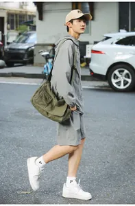 A model carrying a large olive green canvas messenger bag in an outdoor street setting