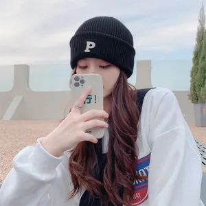 Close-up of a black knitted beanie hat with white letter P embroidery worn by a model