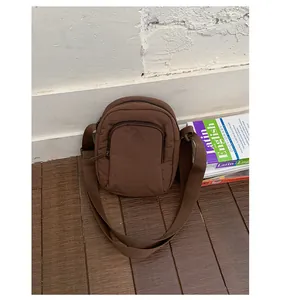 Nahaufnahme einer braunen gesteppten Nylon-Umhängetasche mit geprägtem Logo auf Holzboden.