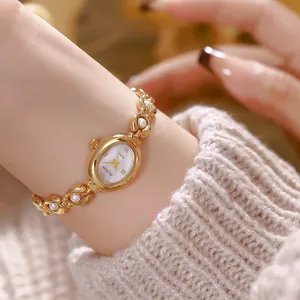 Dettaglio macro di un orologio ovale dorato vintage con bracciale di perle al polso di donna