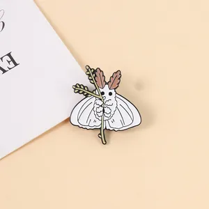 Broche en émail de mite blanche tenant une branche fleurie, accessoire pour sacs et vêtements.