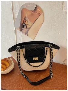 Sac en paille tressée avec rabat en cuir matelassé noir et chaîne dorée sur table