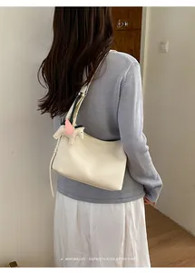 Detail view of a cream minimalist textured underarm shoulder bag featuring a cute Pegasus charm