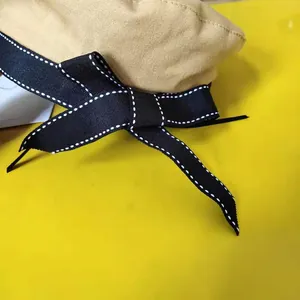 Detail view of beige beret hat featuring a stylish black ribbon bow with white stitching
